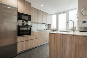 Kitchen with oak furniture, integrated appliances, white stone countertop and dark stoneware floor...