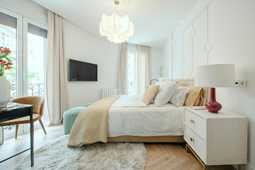 Bedroom with a double bed with light colored cushions, light wood bedside tables and several balconies facing the street
