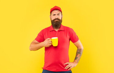 Fototapeta premium Serious bearded man in casual red cap and tshirt holding mug yellow background, tea