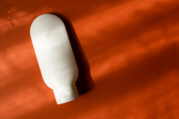 Plastic white tube for cream or lotion. Skin care or sunscreen cosmetic in top view on orange background with beautiful shadows. Beauty concept for face care
