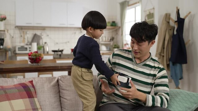 slow motion of surprised Asian dad saying wow while his baby son covering his eyes and giving him a present from behind. Father’s Day celebration at home concept