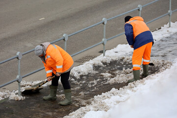 Two workers with shovels cleaning sidewalk, snow and melting ice removal in spring city