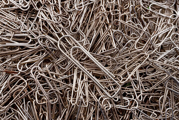 Background of paper clips in steel color. Staples are scattered randomly over the surface.