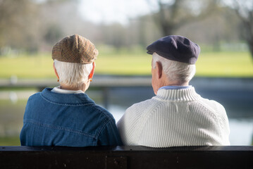 Back view of aged couple spending week end in park. Grey-haired husband and wife resting on bench outdoors, dreaming talking of life, looking far. Happiness, healthy lifestyle of aged people concept