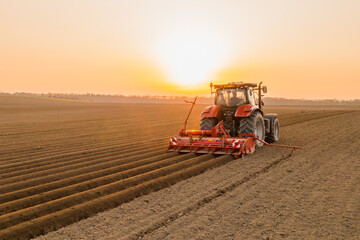 Tractor drives across large field making special beds for sowing seeds into purified soil....