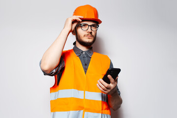 Young construction worker with smartphone in hand on white background.