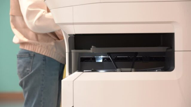 Person using Printer, scanner or laser copy machine. A printed sheet of paper is coming out from the exit of the office printer.