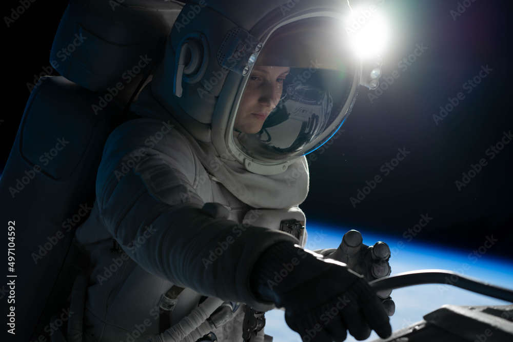 Wall mural female astronaut performing spacewalk, working on a outer part of a space craft