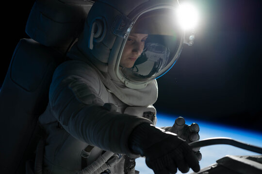 Female astronaut performing spacewalk, working on a outer part of a space craft
