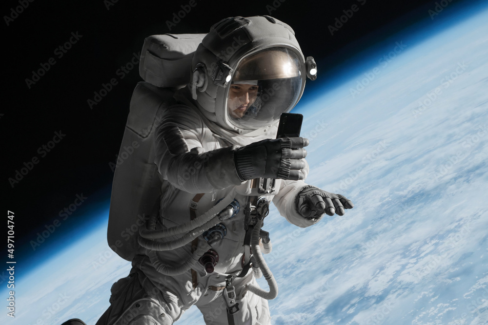 Wall mural female astronaut having a video call on her phone while performing spacewalk in open space, earth in