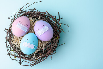 Fototapeta premium Three Easter eggs with eyes with colorful eggs in medical mask covid-19. Easter holidays decoration. Copy space place 