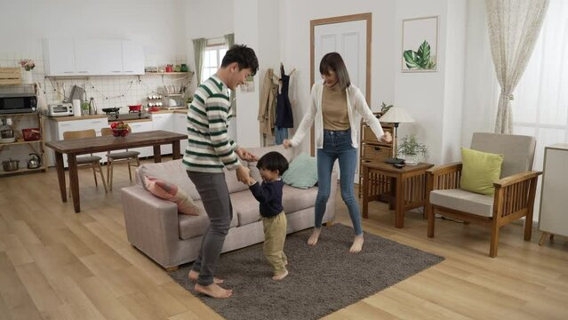 full length shot happy Asian family of three having fun dancing together at home. the baby boy jumping up and down with his father and mother on floor