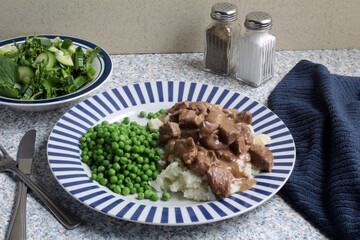Beef in Onion Gravy served over mashed potatoes with peas and salad