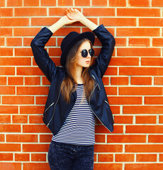 Portrait of stylish young woman model wearing black rock style on brick wall background