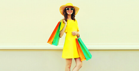 Beautiful happy smiling woman with shopping bags wearing yellow dress and summer straw hat in the city