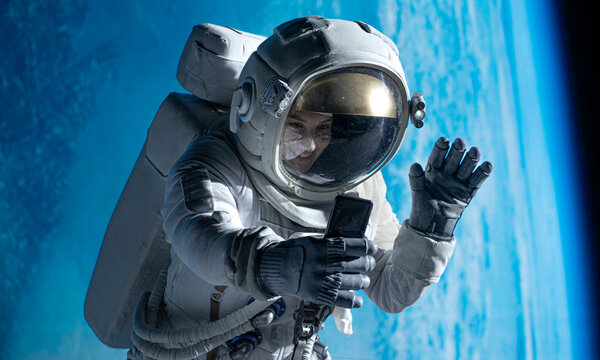 Female astronaut having a video call on her phone while performing spacewalk in open space, Earth in the background - Powered by Adobe