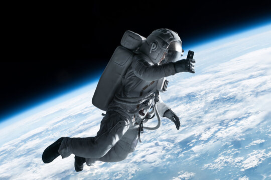 Female astronaut having a video call on her phone while performing spacewalk in open space, Earth in the background