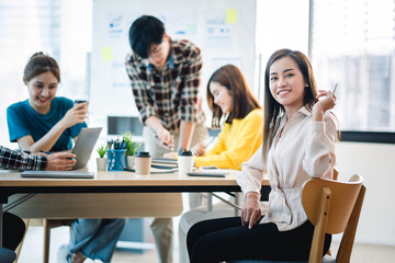 A positive secretary smiles for the camera during a meeting with colleagues working in the background.