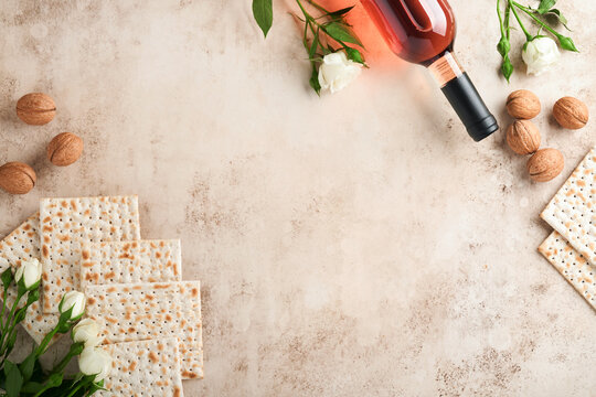 Passover celebration concept. Matzah, red kosher walnut and spring beautiful rose flowers.. Traditional ritual Jewish bread on sand color old concrete background. Passover food. Pesach Jewish holiday.