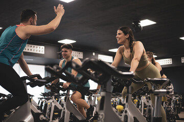 people on bikes in spinning class in modern gym, exercising on stationary bike. group of athletes training on exercise bike - obrazy, fototapety, plakaty