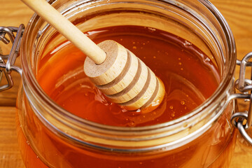 Closeup honey with wooden honey dipper in glass jar