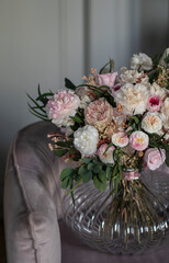Vintage floral composition in glass vase on soft armchair. Bouquet of pink roses, peony flowers and eucalyptus.
