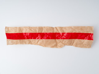 Red tape on crumpled brown wrapping paper. Torn horizontal red sticky tape. Adhesive piece