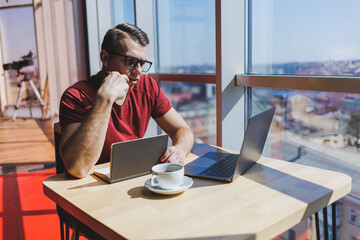 Portrait of a man, IT professional, working remotely with a modern laptop, sitting at a table and...