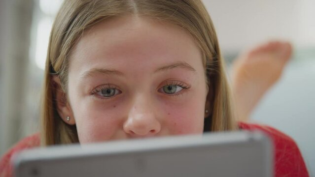 Close up of teenage girl wearing orthodontic braces lying on bed at home looking at screen of digital tablet - shot in slow motion