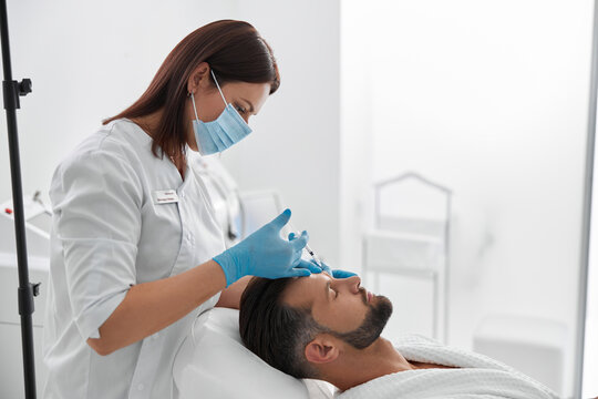 Woman in mask does filler injection for eyebrow lifting to middle aged man in salon