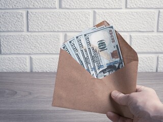 The hand holds a paper envelope with dollar bills. Bonus, reward, benefits concept