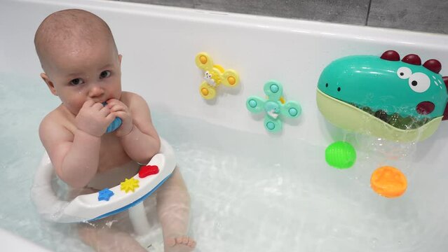 The baby boy bathes in the bathroom sitting in a chair. Happy toddler baby boy bathes in a white bath while sitting on a chair.
