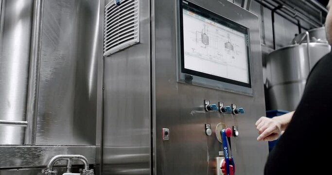 A Person Monitors Production on a Touch Screen Computer in a Manufacturing Facility. Industrial control panel display on the window factory. Modern Beer Factory. Brewery concept. Brewing equipment.