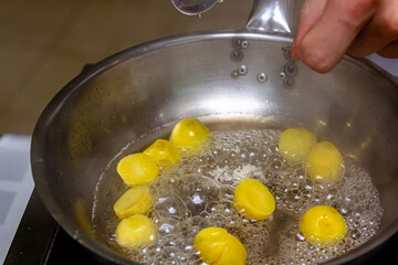 The cook is frying potato balls in a frying pan
