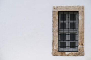 Beautiful window with black grill and an unusual frame on a white wall of an ancient building