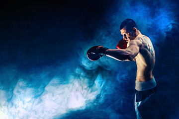 Half length muscular kickbox or muay thai fighter who punching on smoke background. Sport concept.