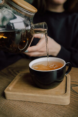 Young woman in cafe during quarantine. Girl pouring some tea from teapot into white cup. Beautiful woman in green sweater smile.