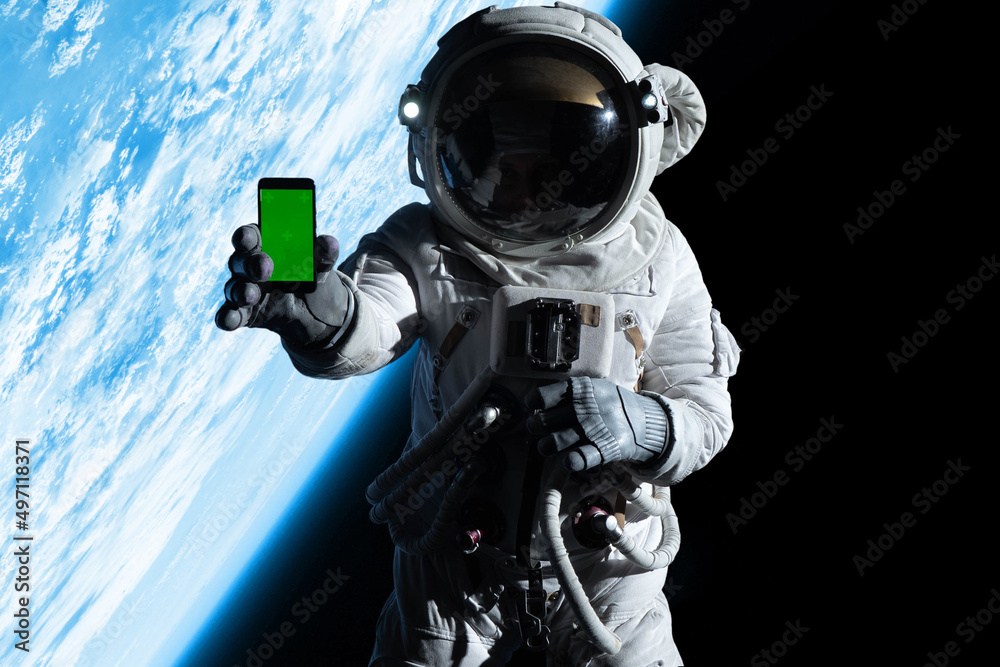 Wall mural astronaut showing a screen of a phone into a camera while performing spacewalk in open space, earth 