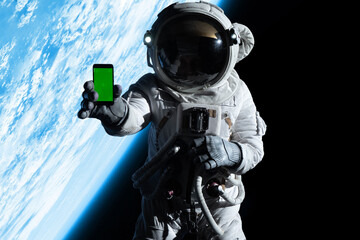 Astronaut showing a screen of a phone into a camera while performing spacewalk in open space, Earth...