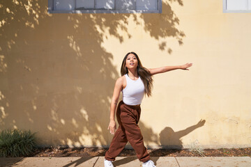 Woman dancing in front of warm beige wall with arm extended to side