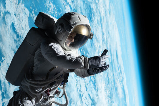 Female astronaut having a video call on her phone while performing spacewalk in open space, Earth in the background