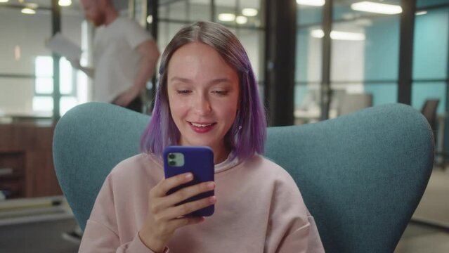A young cute student sits on the chair and reads humorous posts on the Internet, close up slow motion