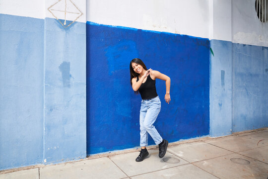 Woman Dancing In Front Of Blue Wall Outdoors With Hand Touching Shoulder