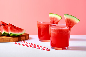 Close-up fresh watermelon juice or smoothie in glasses with watermelon pieces on pink background.