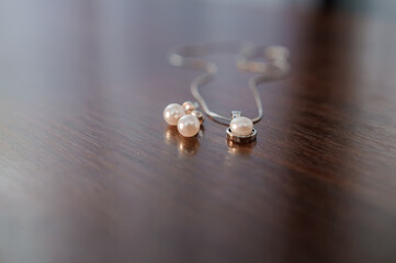 Earrings with pearls, pendant on a chain with pearls on a brown background