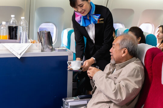 Young Beautiful Asian Flight Attendant Serving Food And Drink To Passengers On Airplane. Stewardess Pushing Food Cart Along Aisle To Serve The Customer. Airline Service Business Concept.