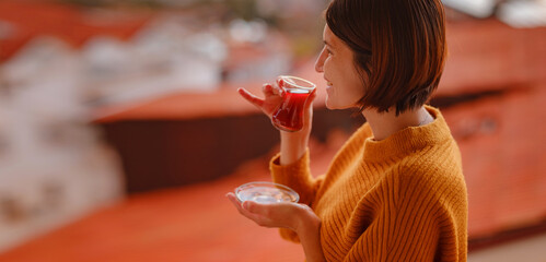 Woman drinking turkish tea from traditional turkish teacup and enjoys panorama over sunset of Kas...