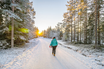 A calm tranquil view of the snow covered trees in the snowdrifts and beautiful sunset. A beautiful woman in coloured jacket walking through the Magical winter forest.