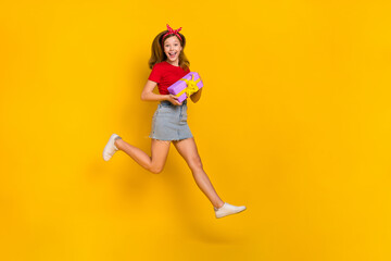 Full body photo of cool little girl run birthday wear t-shirt hairband skirt sneakers isolated on yellow background