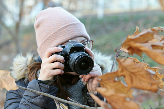 A photographer girl holds a professional photo-video camera in her hands. Against the background of beautiful autumn nature